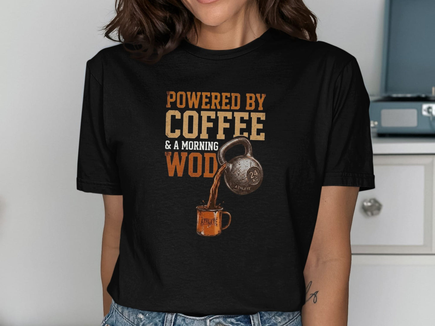 Black t-shirt graphic: "Powered by Coffee & a Morning WOD" with kettlebell pouring coffee into a mug.