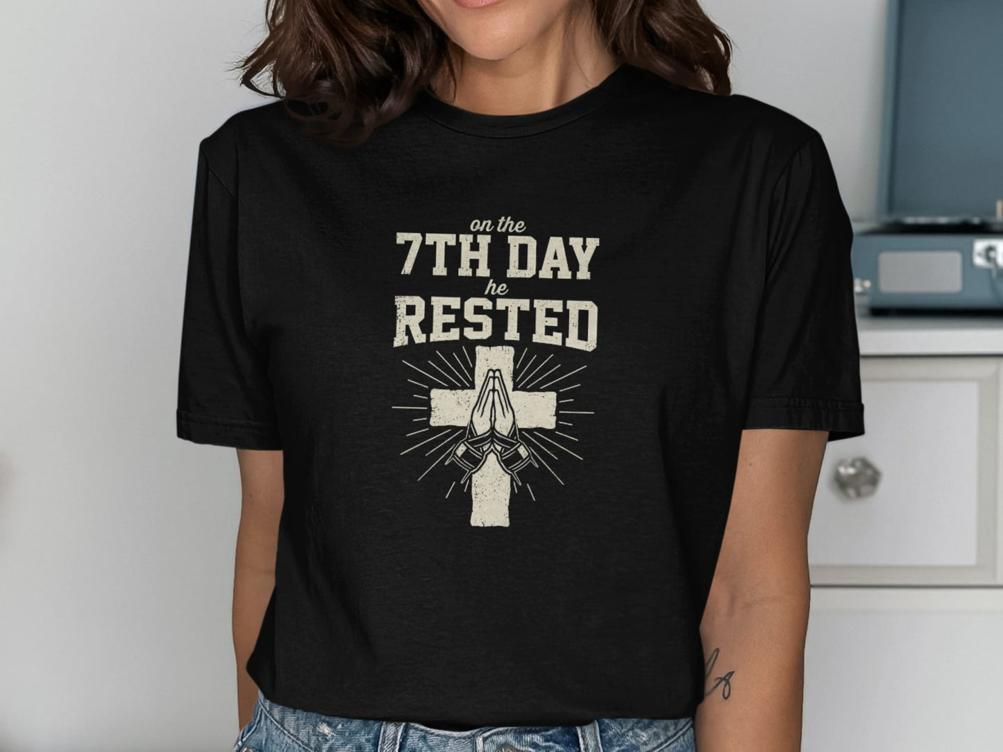 Black t-shirt with "on the 7th DAY HE RESTED" and praying hands with cross.