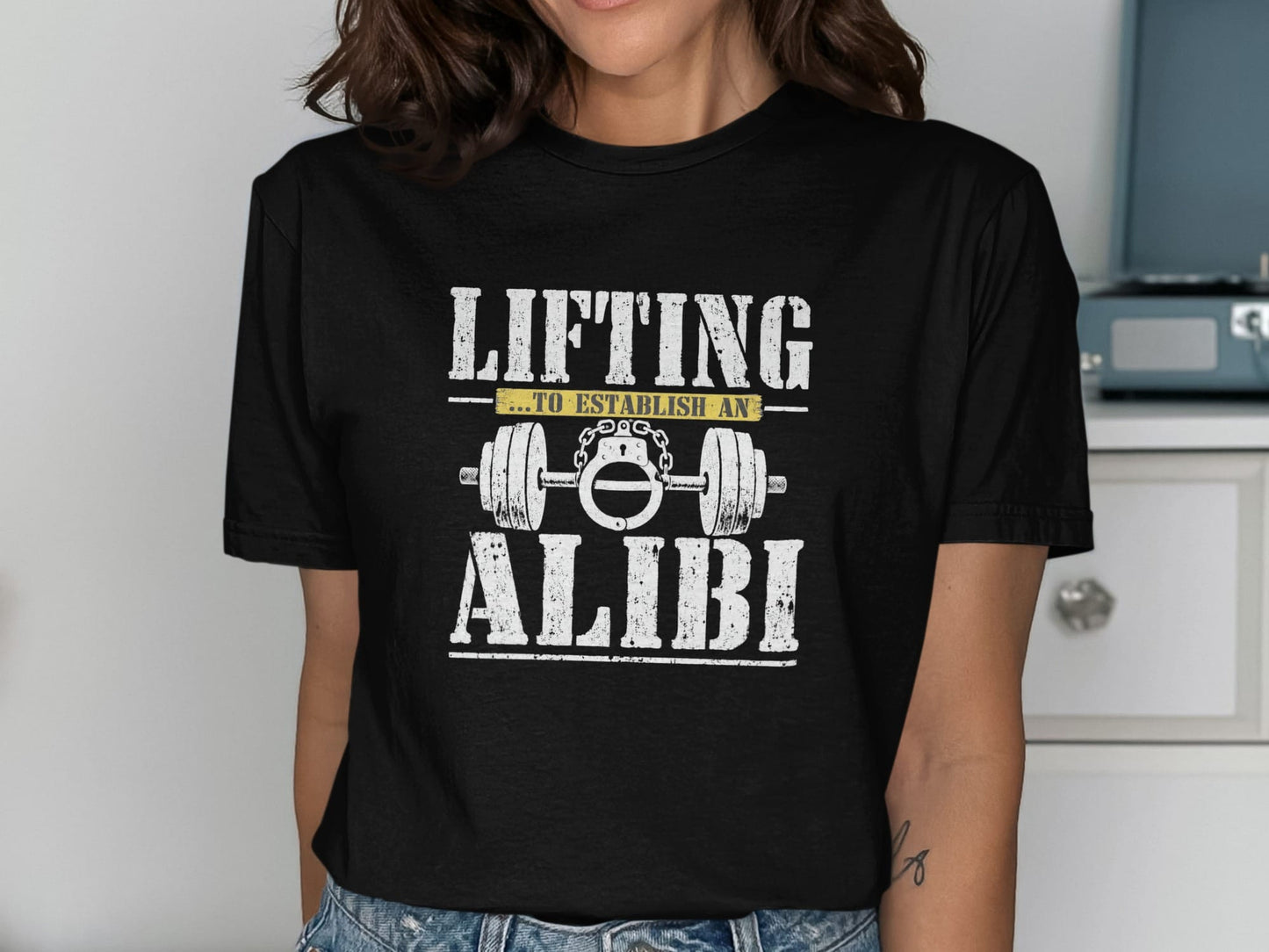 Black t-shirt with white text "LIFTING ...TO ESTABLISH AN ALIBI" and barbell graphic.