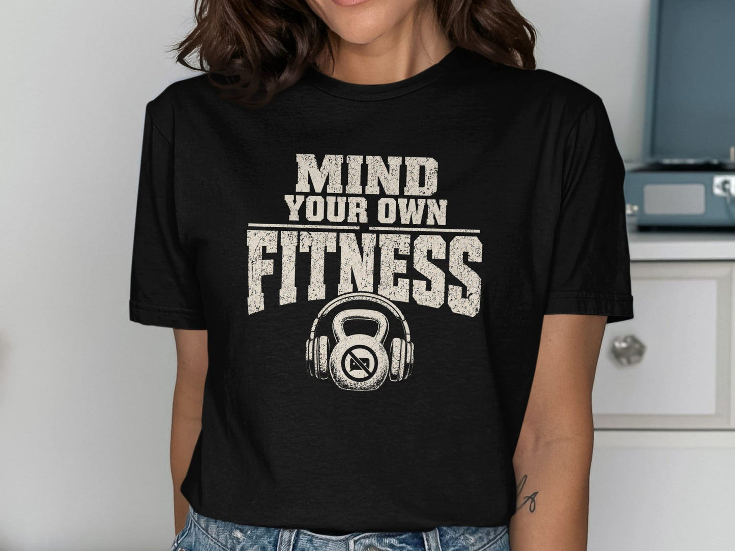 Black t-shirt with "Mind Your Own Fitness" text and kettlebell with headphones graphic.