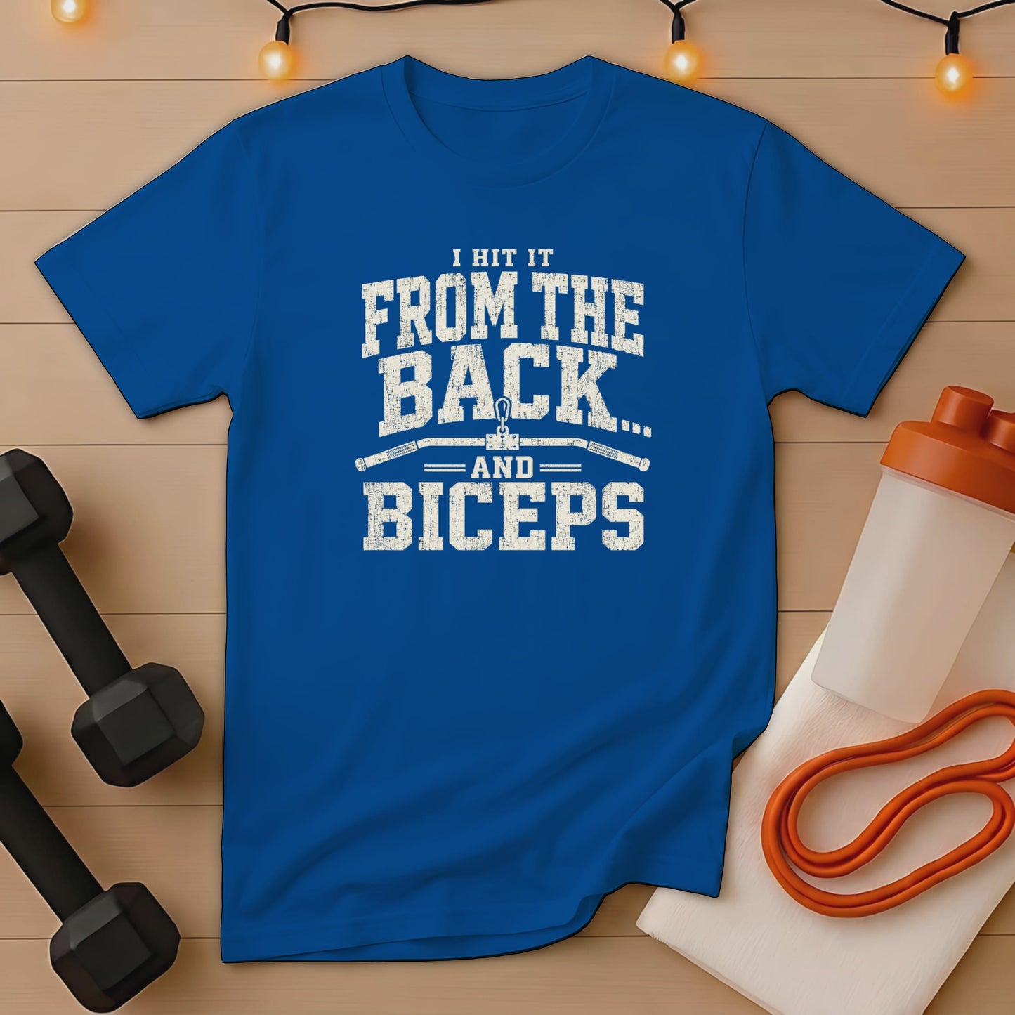 Blue t-shirt with distressed text "I HIT IT FROM THE BACK... AND BICEPS" with gym accessories.